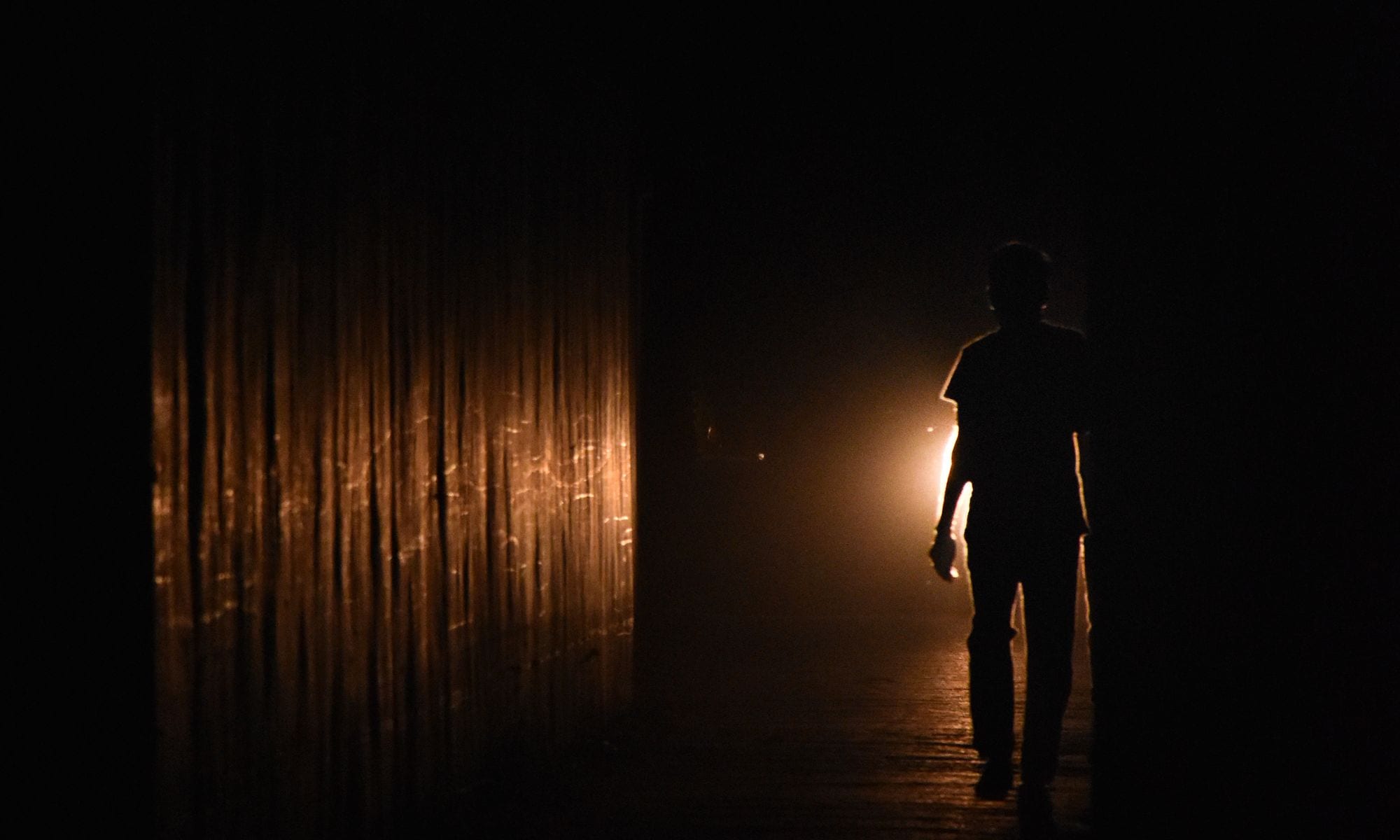 Person als Silhouette, die in einem dunklen Durchgang auf warmes Gegenlicht zugeht.